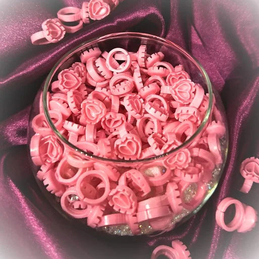 Pink lash glue rings in a glass bowl on a purple satin background