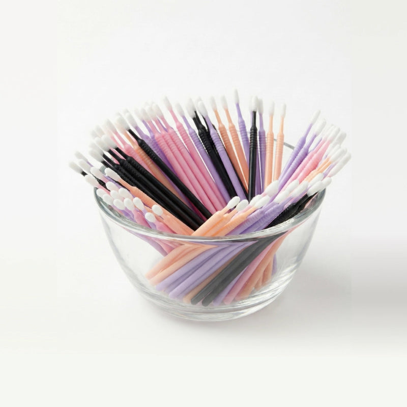 Glass bowl filled with colorful microswabs on a white background