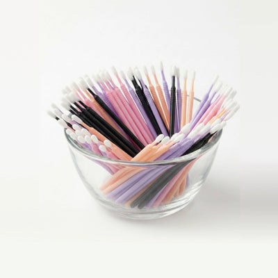 Glass bowl filled with colorful microswabs on a white background