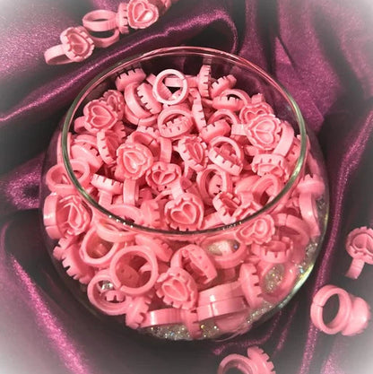 Pink lash glue rings in a glass bowl on a purple satin background